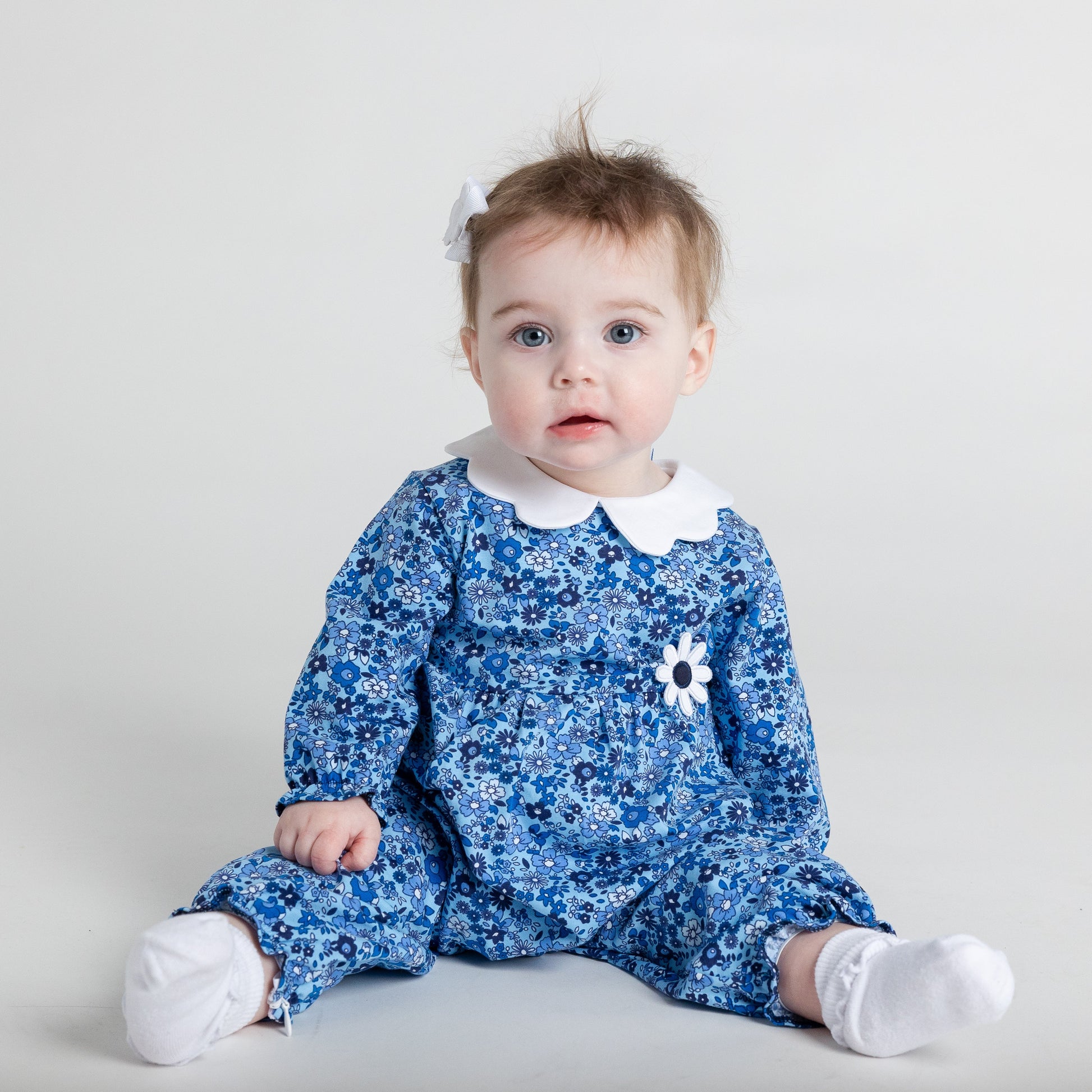 Baby wearing a blue floral romper with a white collar on a light gray background