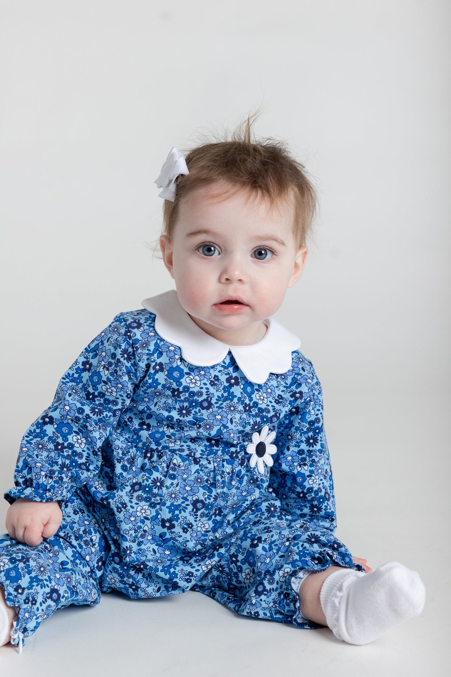 Baby wearing a blue floral romper with a white collar and flower detail on a light gray background